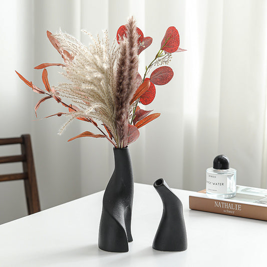 Black vase with dried flowers on a table next to a book and bottle