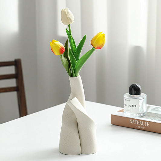 White vase with yellow and red tulips on a table next to a book and perfume bottle.