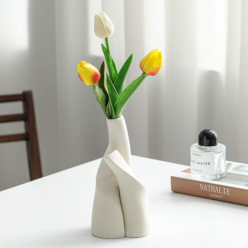 White vase with yellow and red tulips on a table next to a book and perfume bottle.