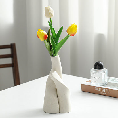 White vase with yellow and red tulips on a table next to a book and perfume bottle.
