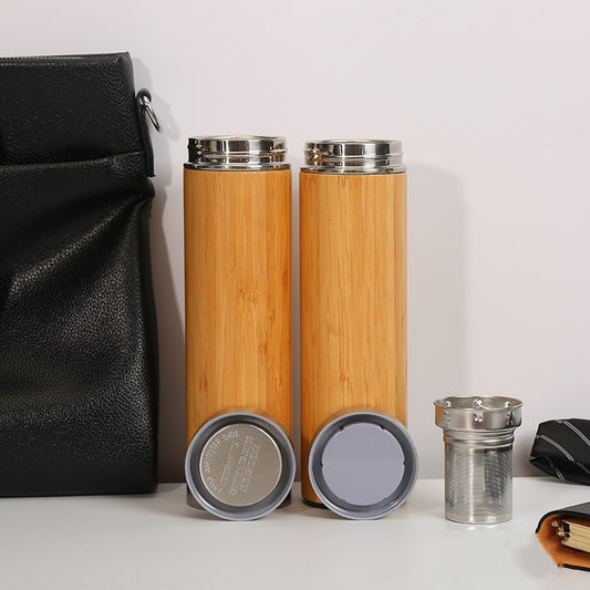 Two bamboo water bottles with silver caps on a white surface next to a black drawstring bag.